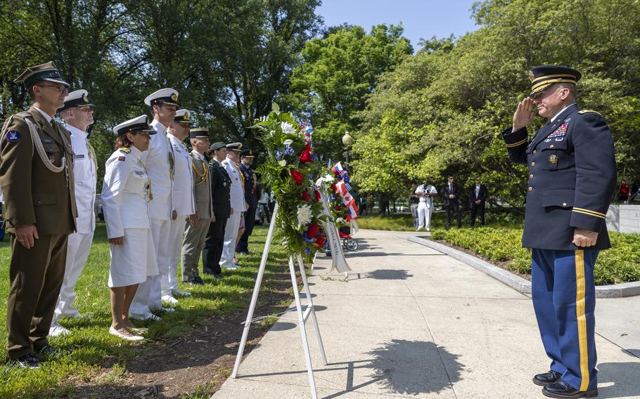 A man in military uniform salutes a wreath that stands before a row of others in uniform.