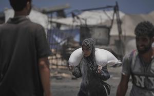 A woman carries a sack of flour over her shoulders.