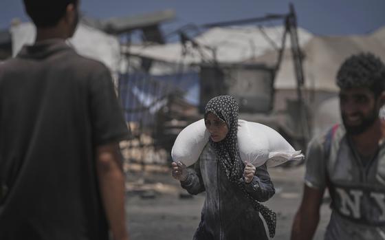 A woman carries a sack of flour over her shoulders.