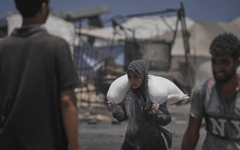 A woman carries a sack of flour over her shoulders.