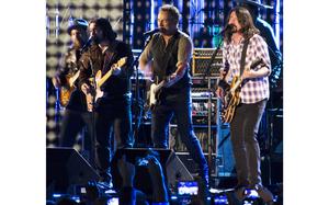 Several people perform on stage, four in the front with guitars and one in the back who is mostly obscured.