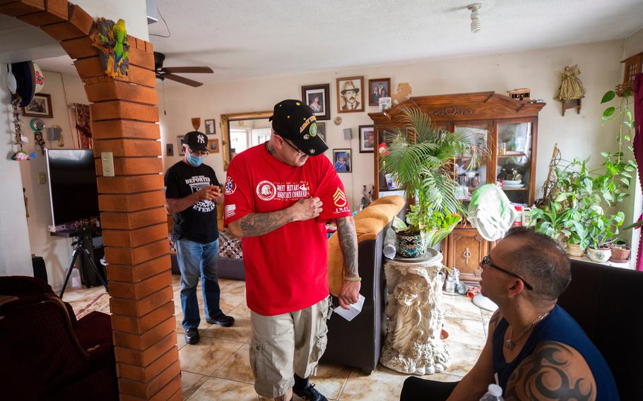 Ivan Ocon, center, a deported veteran who served in the U.S. Army, shows fellow deported veteran, at right, Michael Evans, the emblem on shirts he made for the group of deported veterans.