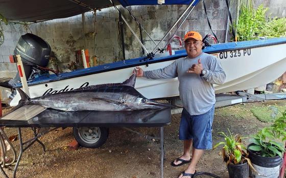 Fisherman  Jeffrey Hattori gives a “hang ten” hand sign as he stands with his hand on the fin of a large fish in front of his small boat, the Lady G.