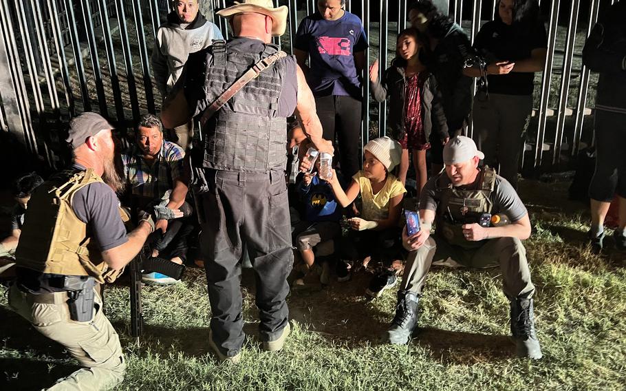 Patriots for America leader Sam Hall, right, talks to migrants as member Shawn Tredway, far left, translates. 