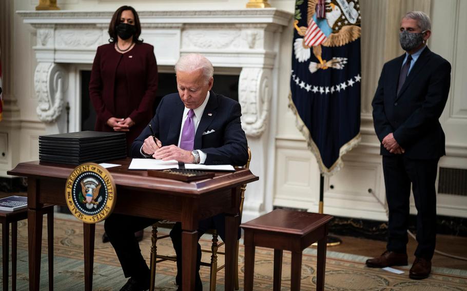 President Biden, with Vice President Harris and director of the National Institute of Allergy and Infectious Diseases Anthony S. Fauci by his side, signs executive orders after speaking about the pandemic in the State Dining Room at the White House on Jan. 21, 2021.