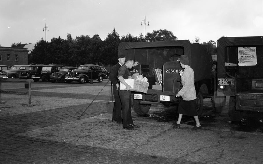 A black and white photo of men taking crates of goods onto or off of the back of a truck.