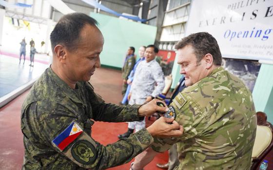 Two men in military uniforms, one pinning a patch on the other’s sleeve.