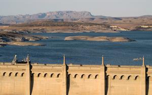 A lake is seen from a distance, with mountains and the horizon in the background and a dam in foreground.