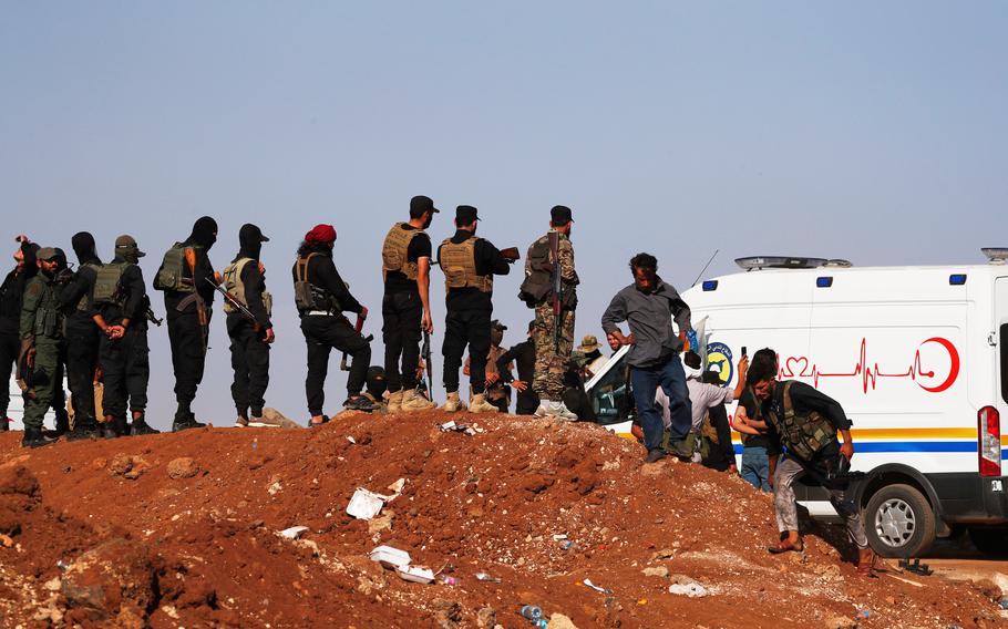 Armed security personnel stand on a ridge, near an ambulance.