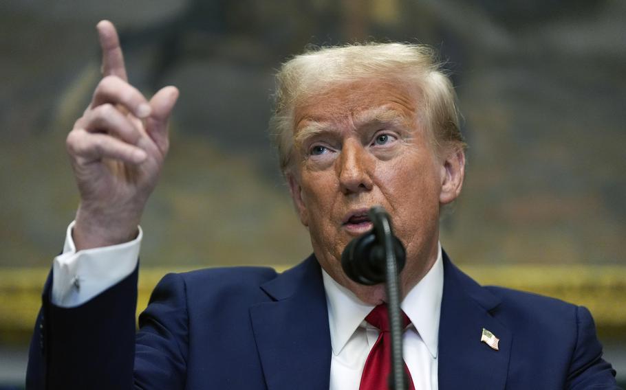 President Trump speaks in front of a microphone with one hand raised, the index finger pointing up.