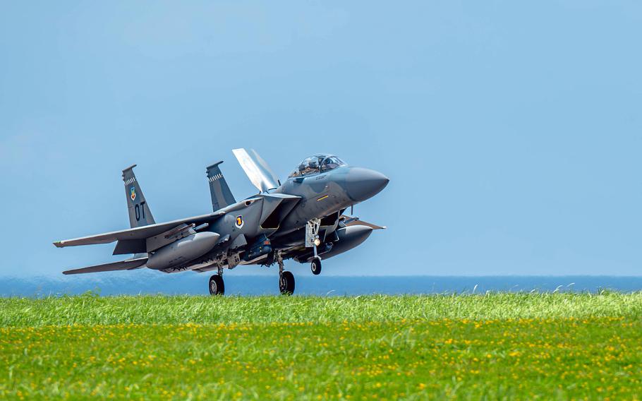 A F-15EX Eagle II lands on a runway, with grass in the foreground and a blue sky in the background.