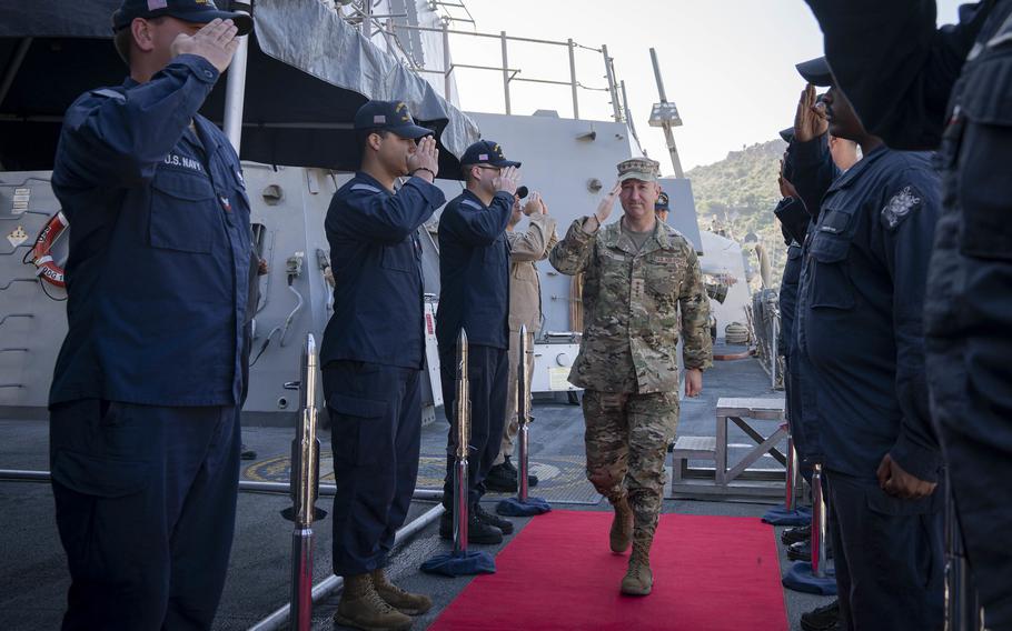 A general salutes sailors as he walks down a red carpet.