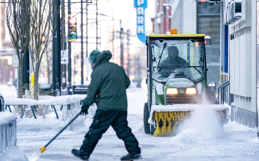 A man shovels the sidewalk while another one clears the snow with a power sweeper Thursday, Dec. 22, 2022, in downtown Minneapolis. 