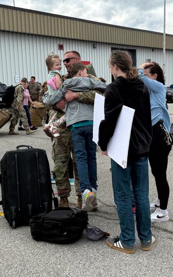 A soldier holds two children while two other family members stand besides him.