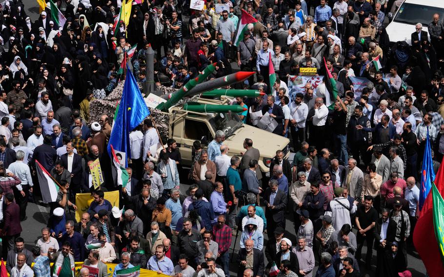 A truck carrying replica missiles in the middle of a square full of people, many carrying flags or banners.