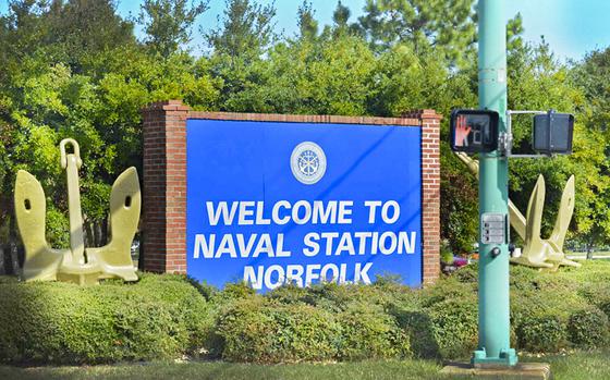 A blue sign, surrounded by bushes and trees, that reads “Welcome to Naval Station Norfolk.”