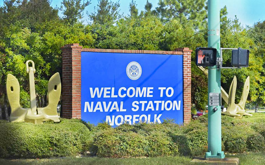A blue sign, surrounded by bushes and trees, that reads “Welcome to Naval Station Norfolk.”