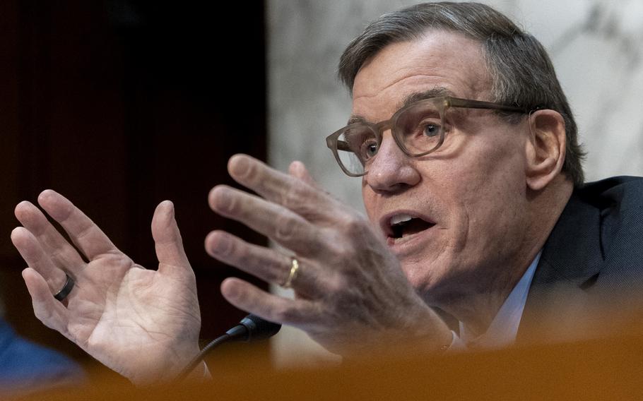 Warner seated and wearing eyeglasses uses both hands as he speaks