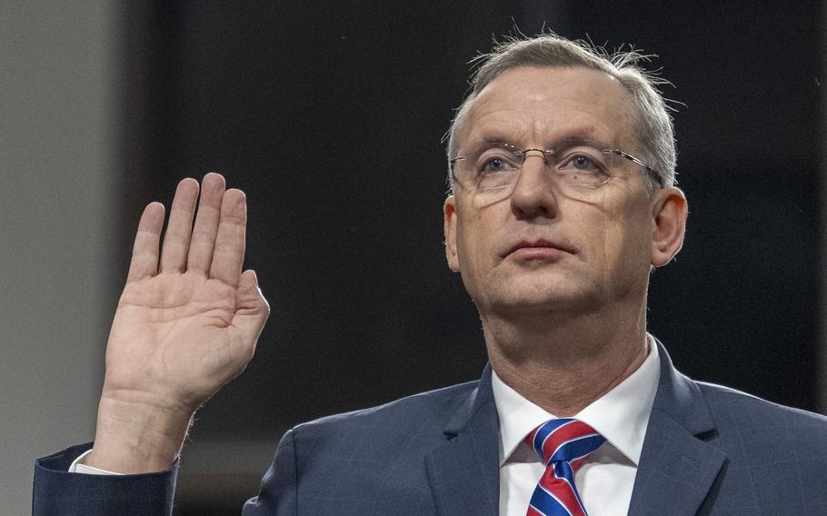 A man in a suit and glasses raises his hand.