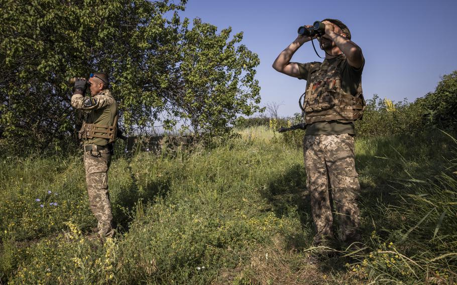 Soldiers use binoculars to scan the sky for Russian drones at an air defense position between Kostyantynivka and Bakhmut on July 5, 2023. 
