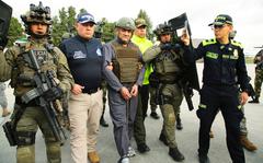 In this photo released by the Colombian Presidential Press Office, police escort Dairo Antonio Usuga, center, also known as "Otoniel," leader of the violent Clan del Golfo cartel prior to his extradition to the U.S., at a military airport in Bogota, Colombia, Wednesday, May 4, 2022.