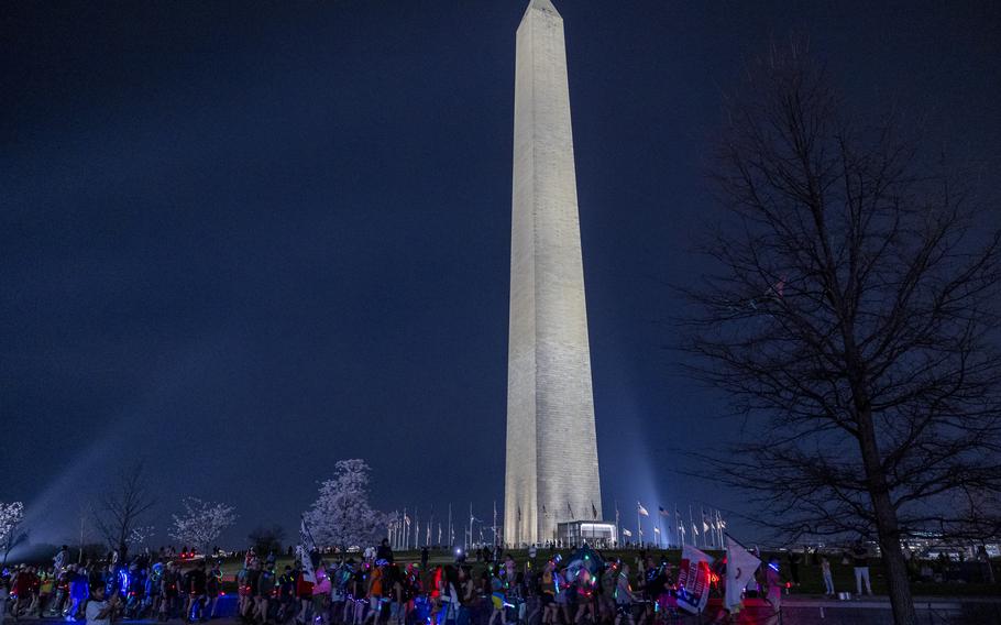 A group of hikers walk past the Washington Monument at night