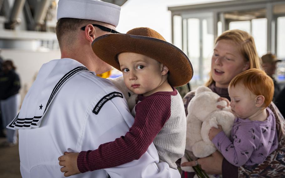 A child wearing a cowboy hat looks at the camera while being carried by a sailor