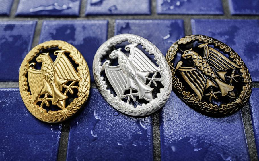 The gold, silver, and bronze variations of the German Armed Forces Badge for Military Proficiency rest poolside at Ramstein Air Base, Germany, as U.S. service members complete the swim test, April 22, 2024. These badges equate to different levels of achievement in the military skills test.