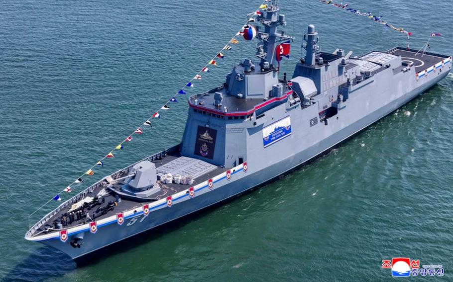 A military warship adorned with North Korean flags, seen from above, transits open water.