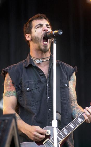 A vertical photo of a man holding a guitar singing into a standing microphone.