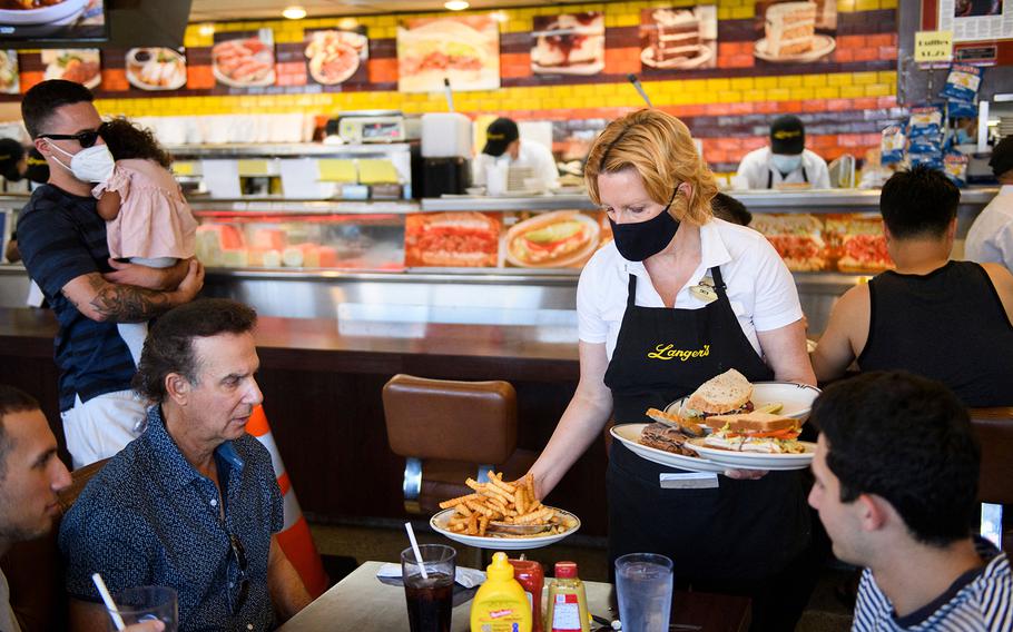 A waiter serves food to customers dining indoors at Langer's Deli in Los Angeles, Calif., on Aug. 7, 2021. 