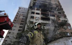 A firefighter at the base of a building gestures; the building towering above him is plainly damaged.