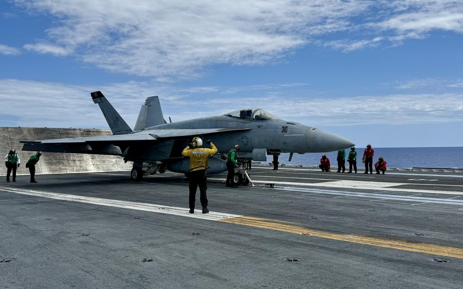 Sailors on an aircraft carrier flight deck wave on a fighter jet on the runway.