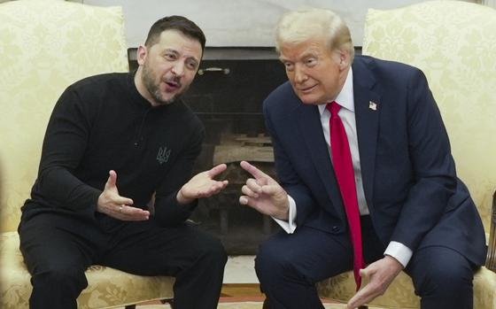 Donald Trump and Volodymyr Zelenskyy lean toward each other while seated side-by-side in yellow chairs in front of a fireplace.