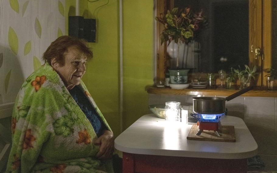An elderly woman cooks food on a gas burner during a blackout in Kyiv, Ukraine, Monday, Nov. 14, 2022. 