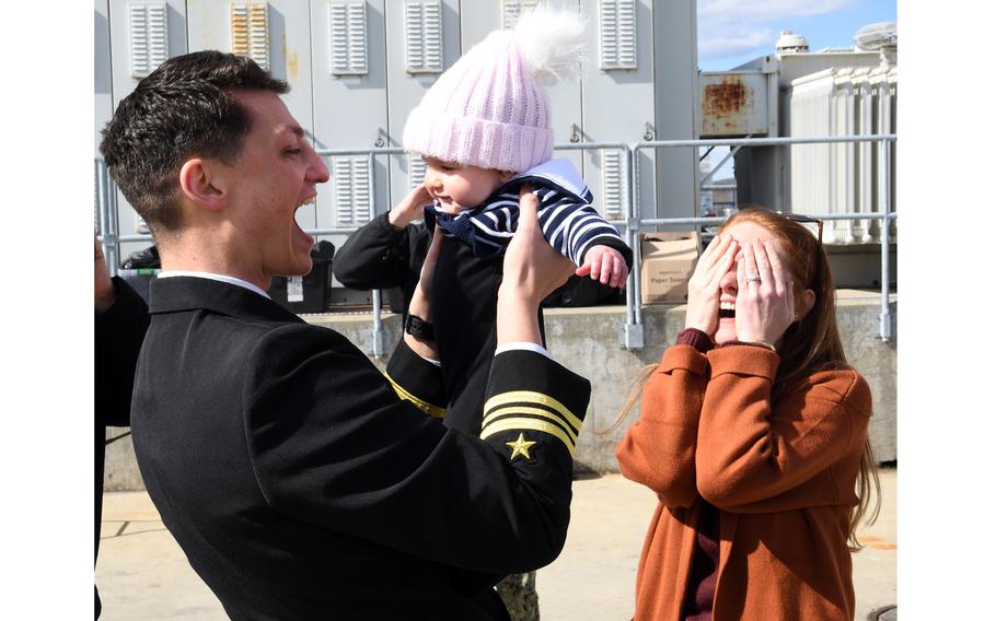 A sailor holds his child with his wife nearby.