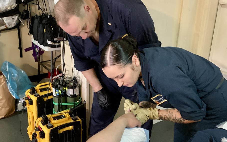 Cmdr. Martin Boese, assigned to an Expeditionary Resuscitative Surgical System team deployed on USS Hershel "Woody" Williams, supervises as Corpsman Kayle Newberry practices putting an IV into the hand of a sailor on May 3, 2024.