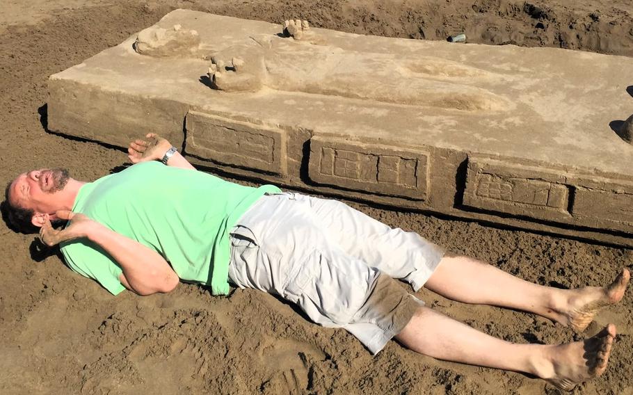 A man lies next to a sand sculpture of Han Solo from “Star Wars: The Empire Strikes Back.”