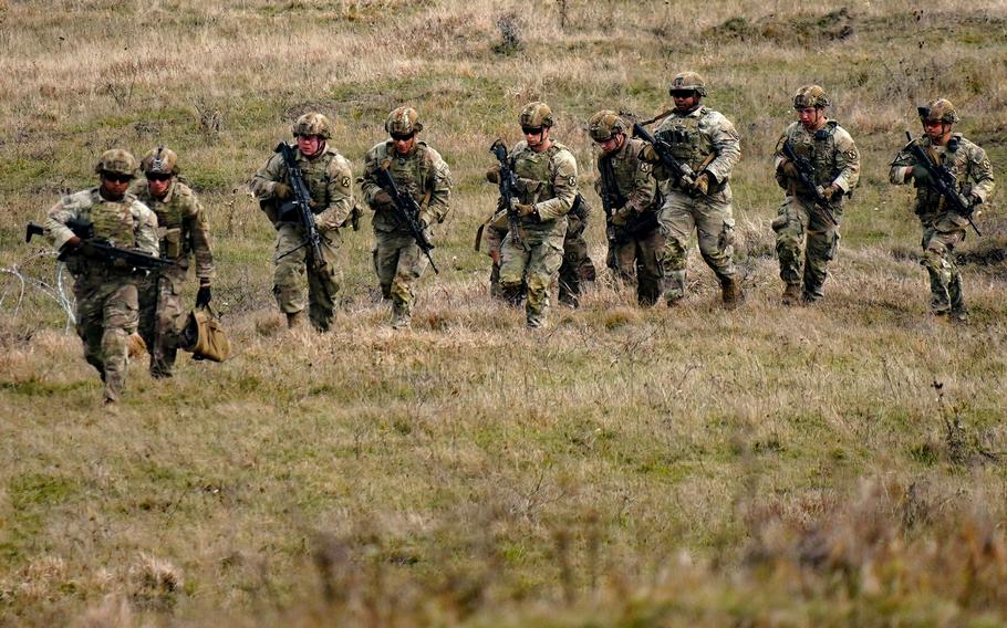 Nine soldiers in uniform walk through a field in Romania. 