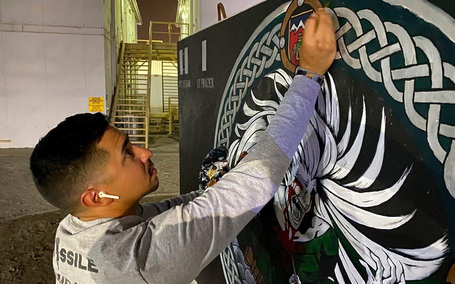 U.S. Army Sgt. Anthony Castillo, a mobility specialist assigned to the 3-157th Field Artillery unit and Colorado National Guard, paints a t-wall with his unit’s adopted patch, April 20, 2022, at Al Dhafra Air Base, United Arab Emirates. To avoid temperatures of 120 F or more, Castillo would gather his painting supplies, don a headlamp and begin painting at night. “The Banshee Barricade” took a total of 33 hours over the span of 20 days to finish.