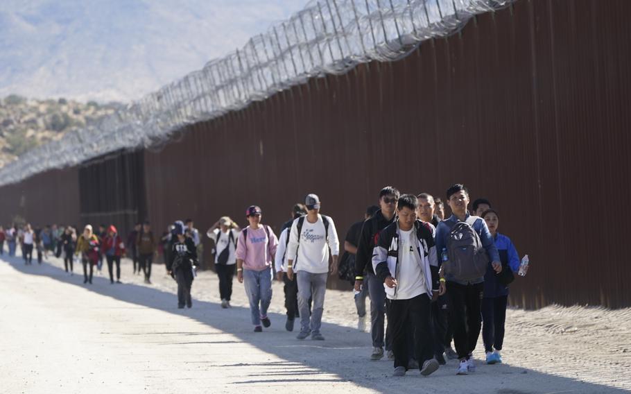 A group of people, including many from China, walk along the wall after crossing the border with Mexico to seek asylum, Oct. 24, 2023, near Jacumba, Calif. 