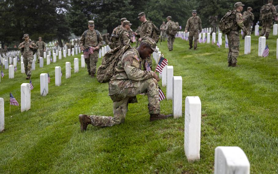 A soldier kneels in front of a headstone, using his boot to measure the spot where he will place a flag.