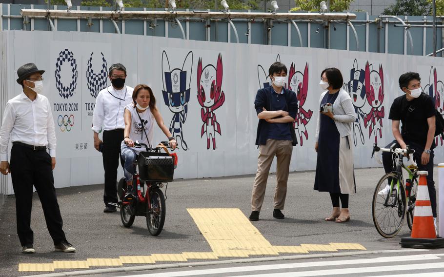 People stand by posters to promote the Tokyo Olympic Games, scheduled to start in the summer of 2021, in Tokyo on Monday, May 24, 2021. 