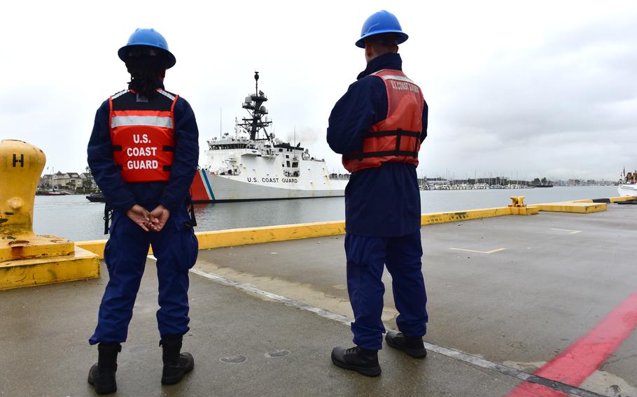 Two service members standing on a dock watching a ship come into port.