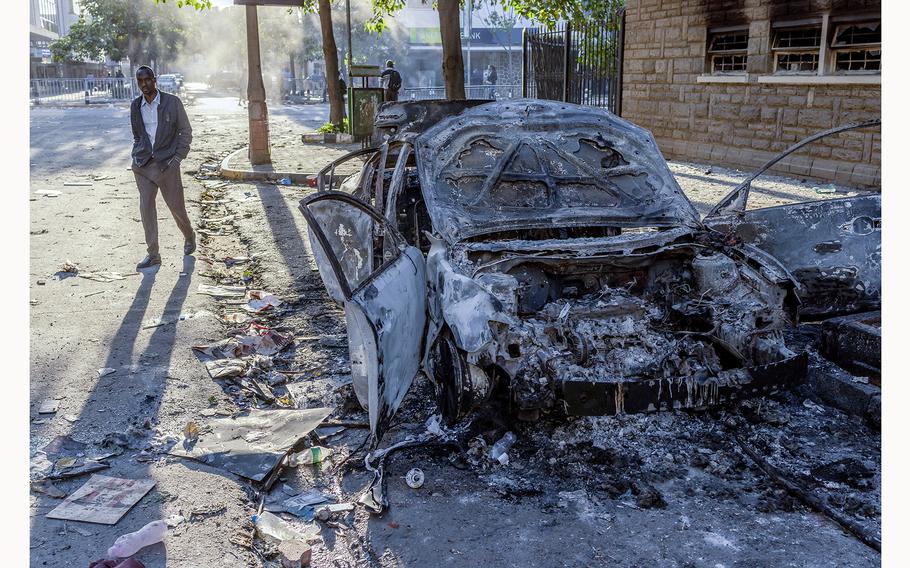 A man walks past the wreckage of a car burned down by protesters in downtown Nairobi, on June 26, 2024, following a deadly nationwide strike to protest against tax hikes and the Finance Bill 2024. Kenya was in a state of shock Wednesday following unprecedented scenes that left parts of parliament ablaze and gutted, as protests over proposed tax hikes turned deadly, prompting President William Ruto’s government to deploy the military. 