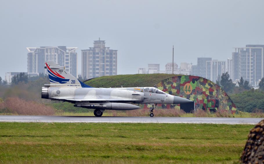fighter jet on tarmac with hangar and a city skyline visible in background 