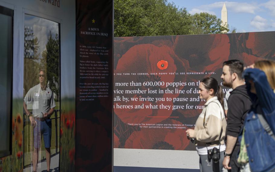 Visitors look at an exhibit/display with the top of the Washington Monument visible in the distance.
