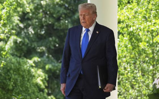 President Trump, wearing a suit and blue tie, walks outside the White House with a binder tucked under his arm.