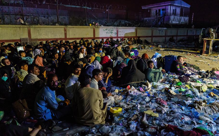Afghan refugees crouch in a group as British military secure the perimeter outside the Baron Hotel, near the Abbey Gate, in Kabul, Afghanistan, on Thursday, Aug. 26, 2021. 