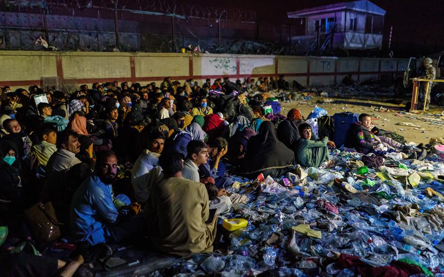 Afghan refugees crouch in a group as British military secure the perimeter outside the Baron Hotel, near the Abbey Gate, in Kabul, Afghanistan, on Thursday, Aug. 26, 2021. 